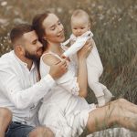 A joyful family with a baby relaxing outdoors in a field during summer.